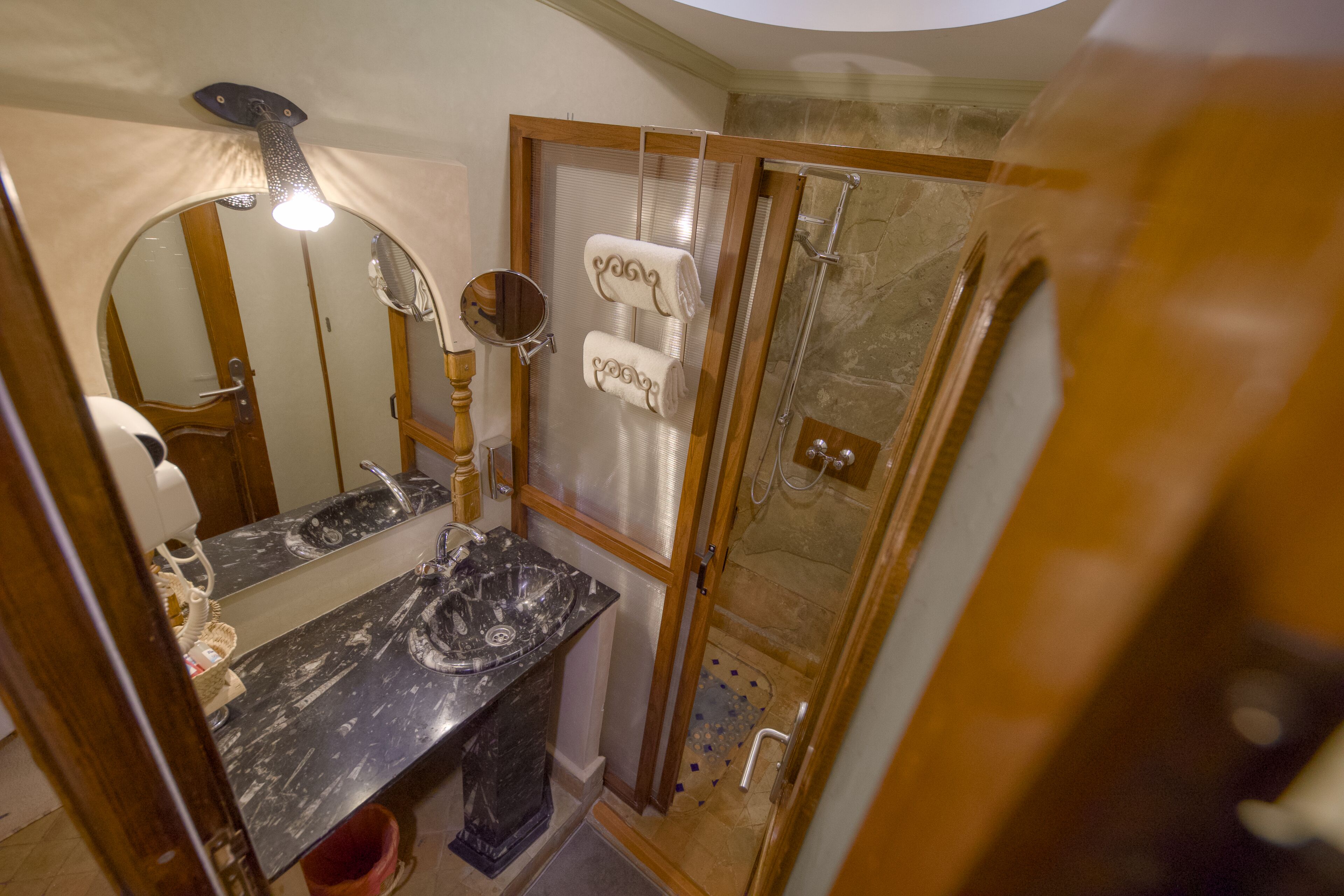 Un baño con lavamanos de mármol, cabina de ducha con mampara de vidrio y puerta de madera.