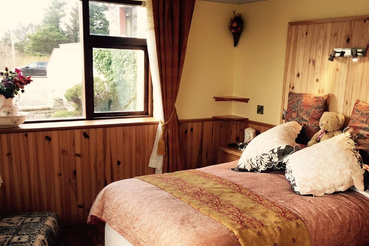 A bedroom with a wooden bed, a window with curtains, a bedside table with a vase, and a red rug.