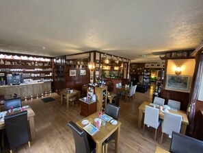 A restaurant with wooden flooring, multiple dining tables, chairs, and a bar area with shelves of bottles and glasses. - Kylemore Pass Hotel (Kylemore)