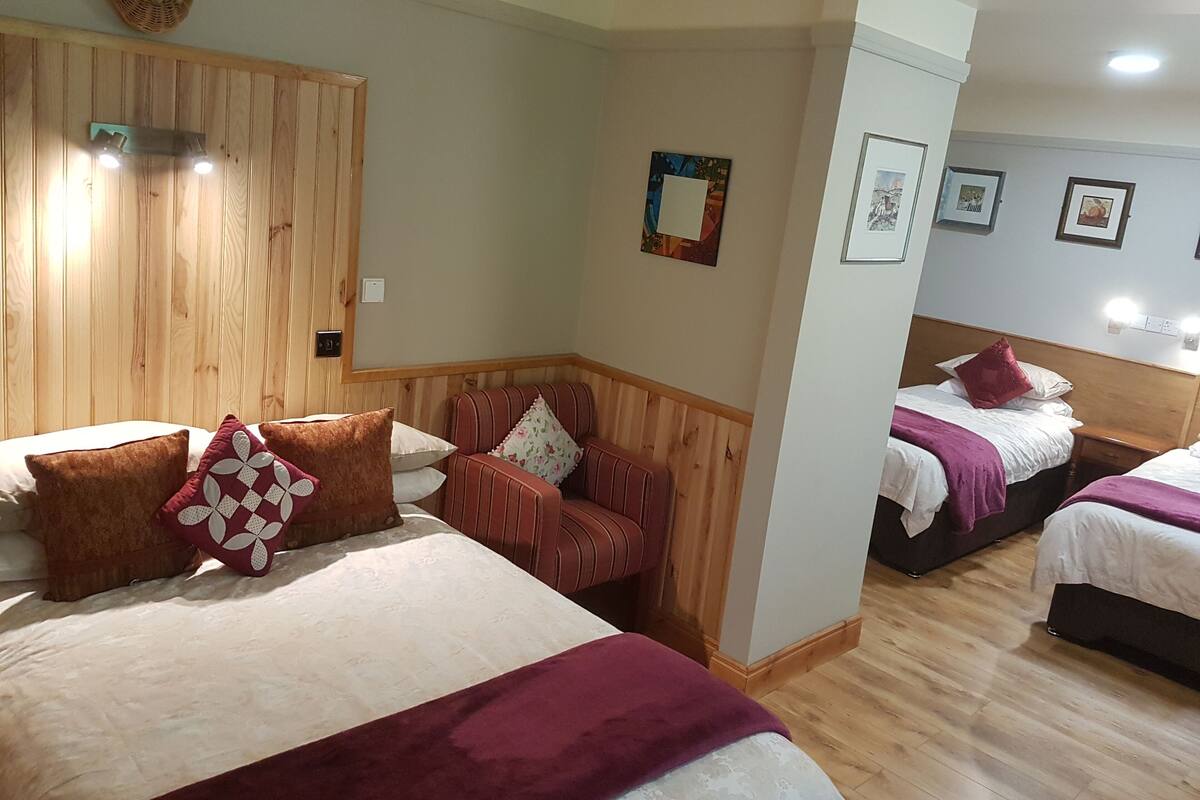 A hotel room with two beds, a wooden headboard, a corner sofa, and a wall with framed pictures.