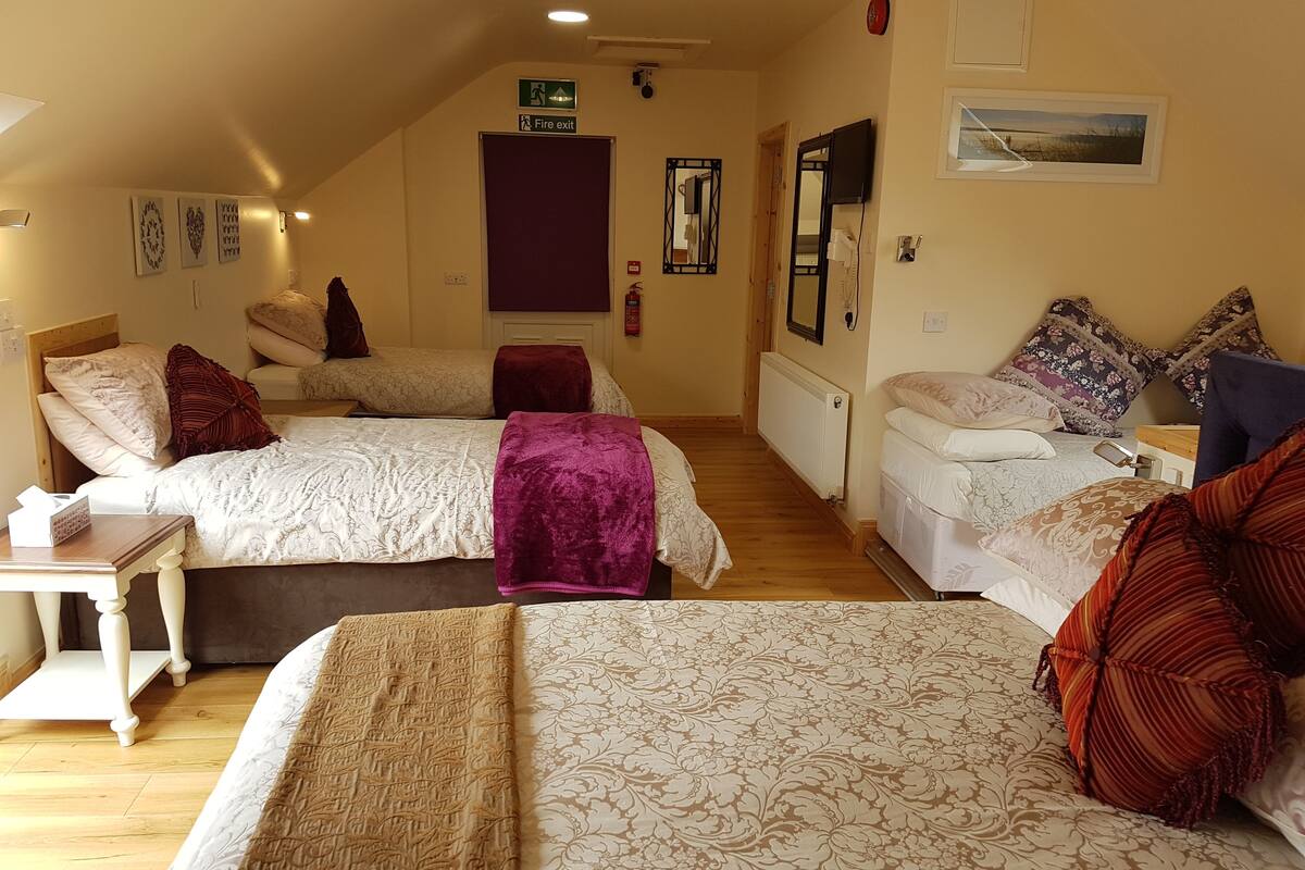 A hotel room with two beds, a small table, a mirror, a fire exit sign, and a framed picture on the wall.