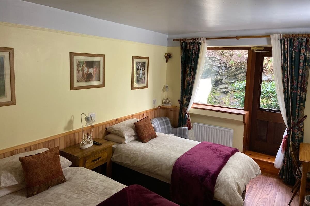 A hotel room with two beds, a wooden headboard, a window with curtains, and a radiator.