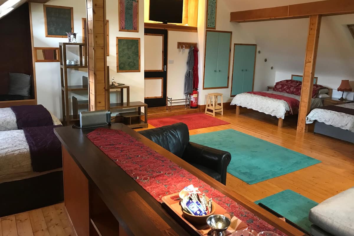 A spacious room with a long wooden bench, a small table with snacks, and two beds with red and white bedding.