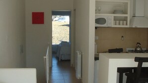 Un couloir étroit mène à une chambre à coucher équipée d’un lit et d’une fenêtre. On peut apercevoir une petite cuisine avec un four à micro-ondes, une cuisinière et des placards.