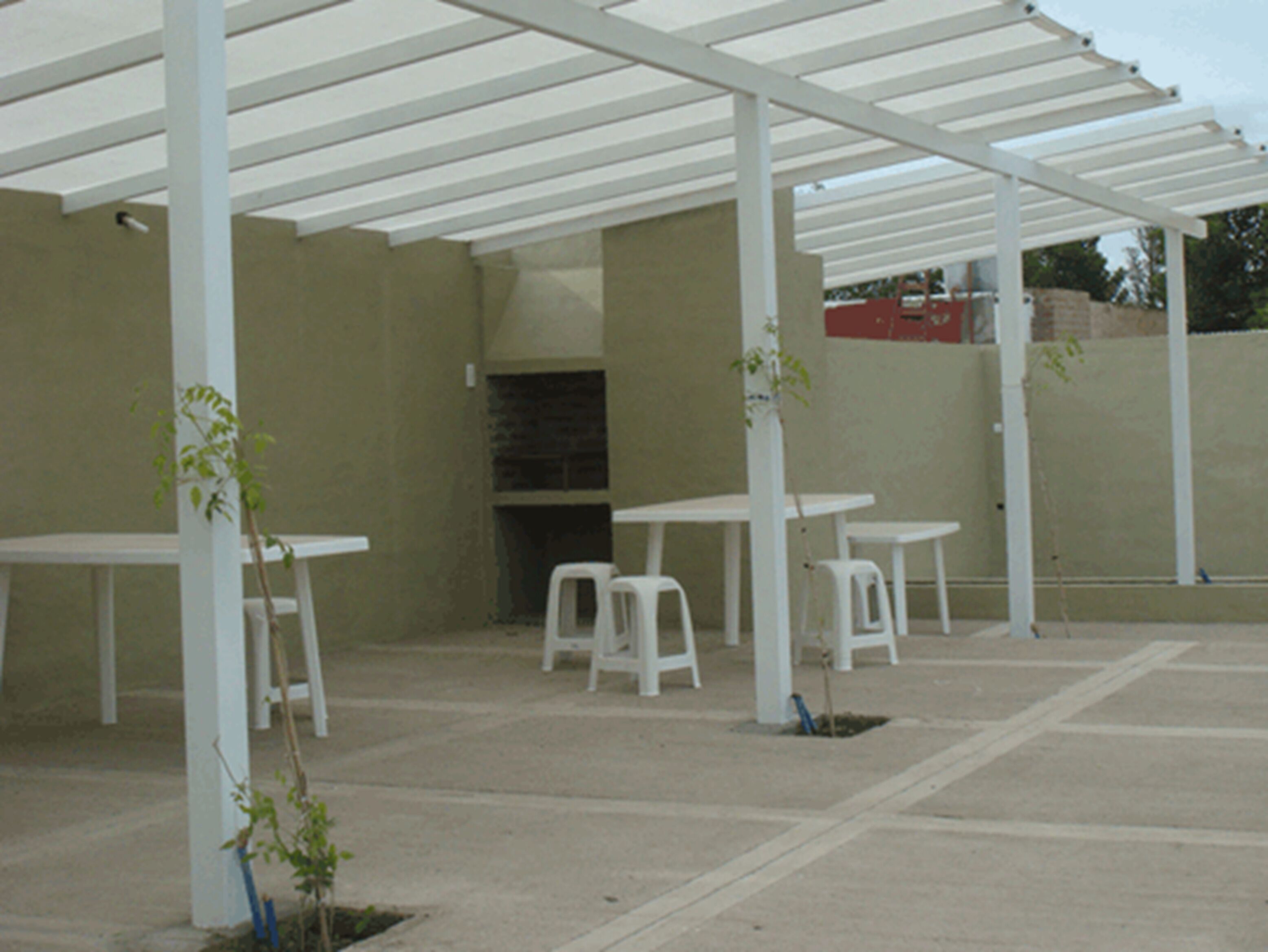 Un espace extérieur aménagé en terrasse, avec des tables et des chaises blanches, une pergola et un four en briques.