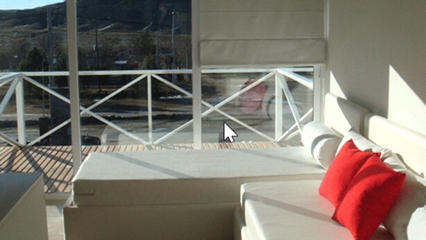 Un balcon avec une balustrade blanche, un canapé blanc agrémenté de coussins rouges et une vue sur un paysage montagneux.