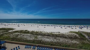 A beach with rows of blue lounge chairs and umbrellas, a sandy beach area, and a clear blue sky. - ~ Two Bedroom @ Phoenix V (Orange Beach)