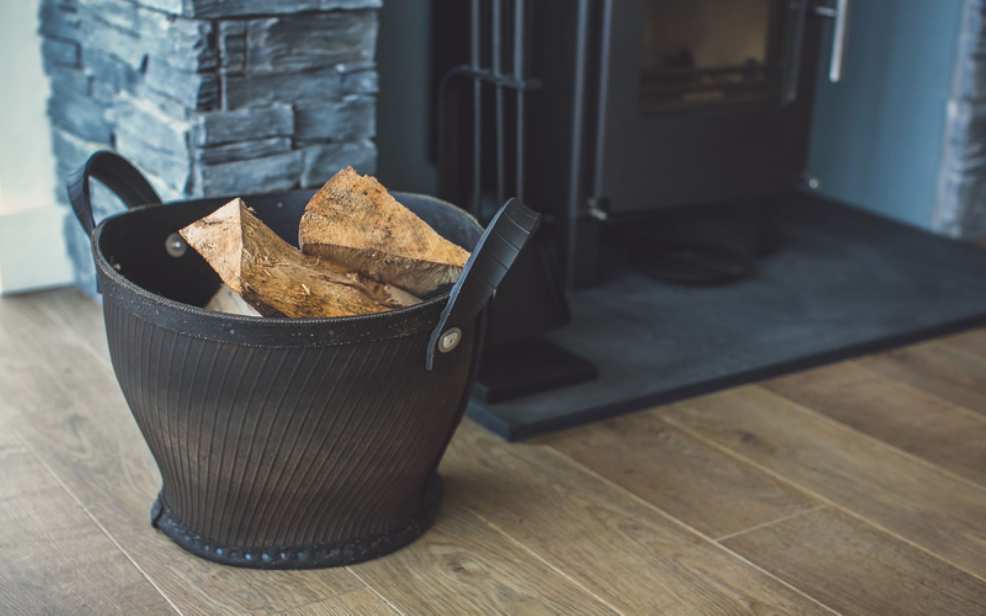 A metal bucket with handles containing breadsticks on a wooden floor.