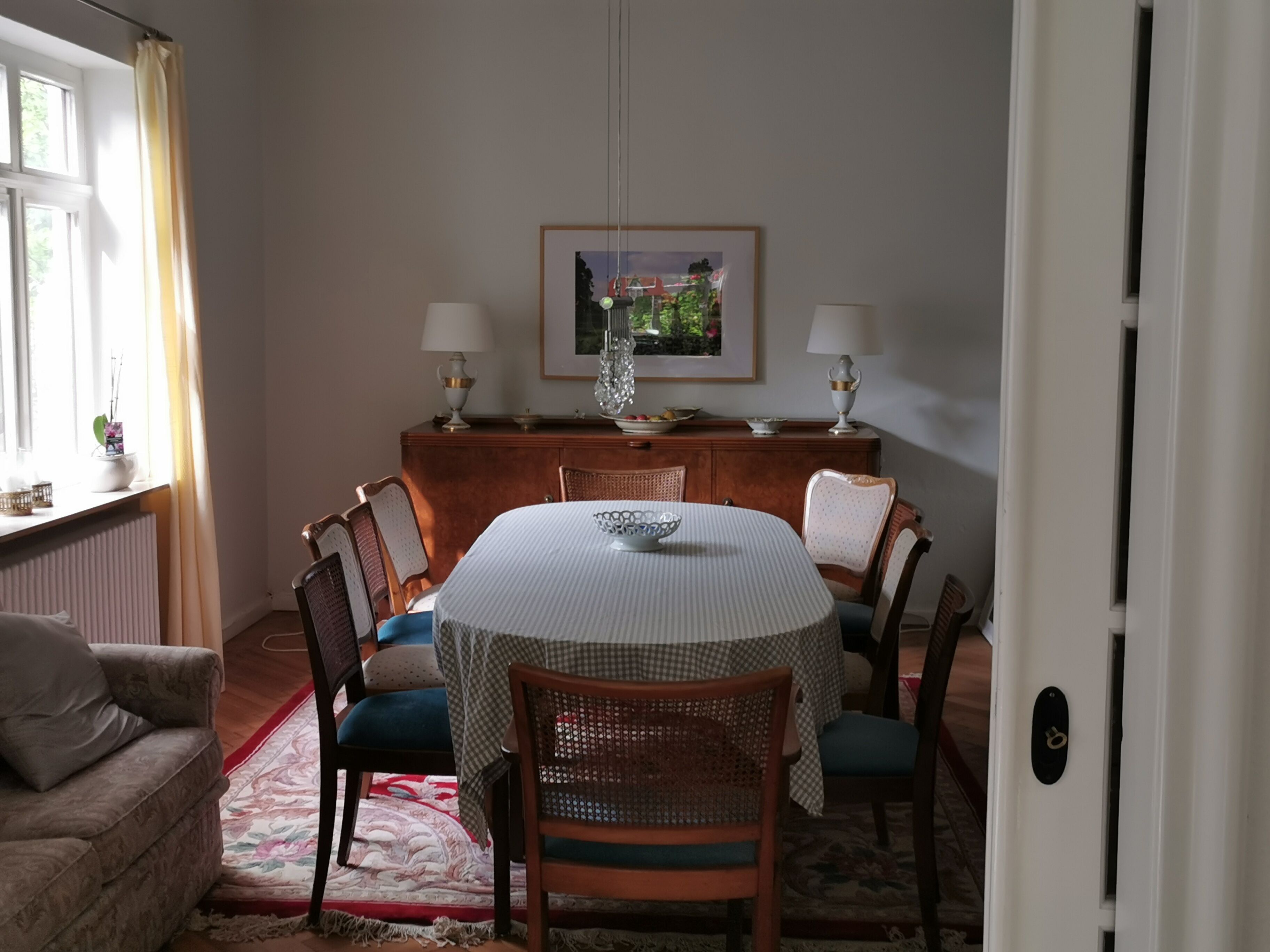 Une salle à manger avec une table ronde, des chaises, un buffet et un tableau encadré au mur.