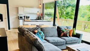 A modern living room with a grey sectional sofa, a wooden coffee table, and a view of a balcony with a deck.
