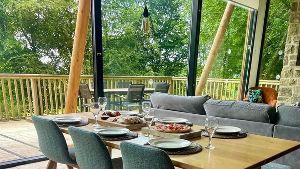 An outdoor dining area with a wooden table, grey upholstered chairs, and a grey sofa.