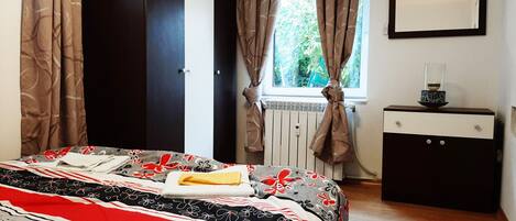 A bedroom with a bed, a dresser, a window with curtains, and a radiator.
