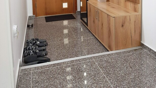 A hallway with a wooden door, a mirror, a black shelf, and a tiled floor.