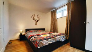 A bedroom with a bed, a nightstand, a wall-mounted deer head decoration, and a window with curtains.