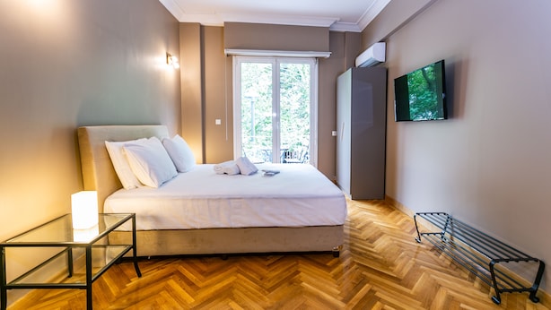 Een slaapkamer met een bed, een glazen tafel, een televisie en uitzicht op groen.