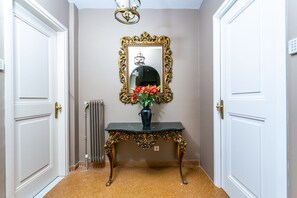 Un couloir avec une console noire, un miroir encadré d’or et un vase rempli de fleurs rouges.