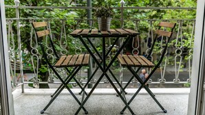 Een balkon met een kleine tafel en twee stoelen, een bloempot op de tafel en een metalen hekwerk.