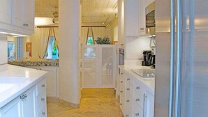 A modern kitchen with white cabinetry, a stainless steel sink, and a visible coffee machine. - Emerald Beach 4 - Villa Plumbago (Gibbes)