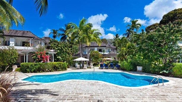 A swimming pool surrounded by lush greenery and palm trees, with houses in the background. - Emerald Beach 4 - Villa Plumbago (Gibbes)