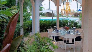 An outdoor dining area with a round table set for four, surrounded by white chairs. - Emerald Beach 4 - Villa Plumbago (Gibbes)