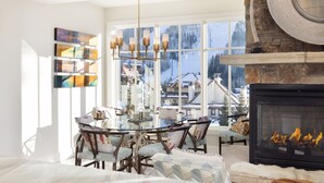 A modern living room with a fireplace, a glass dining table, and a view of a snowy landscape through large windows. - Landmark 517 - 2 Bedroom Diamond (Vail)