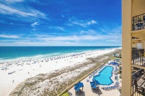 A beach view from a hotel balcony with a pool and lounge chairs.