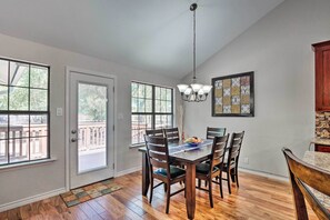 Un comedor con mesa y sillas de madera, ventanas amplias y una lámpara de araña.