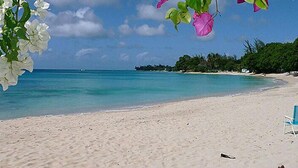 A beach with a clear view of the ocean, a sandy shore, and a blue chair.