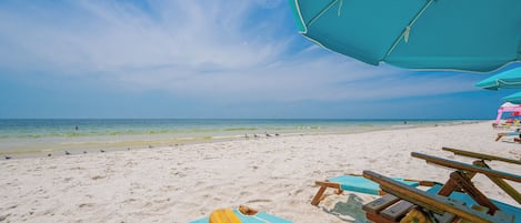Una playa con cielos despejados, una orilla arenosa y sillones de madera.