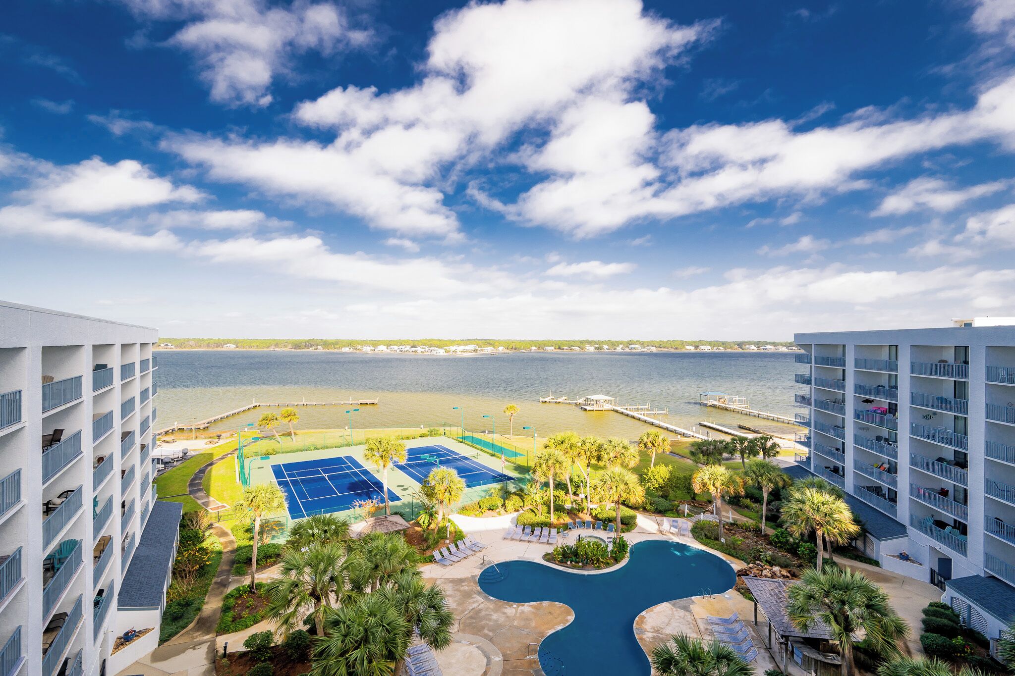 A hotel with a pool, tennis courts, and a view of the sea.