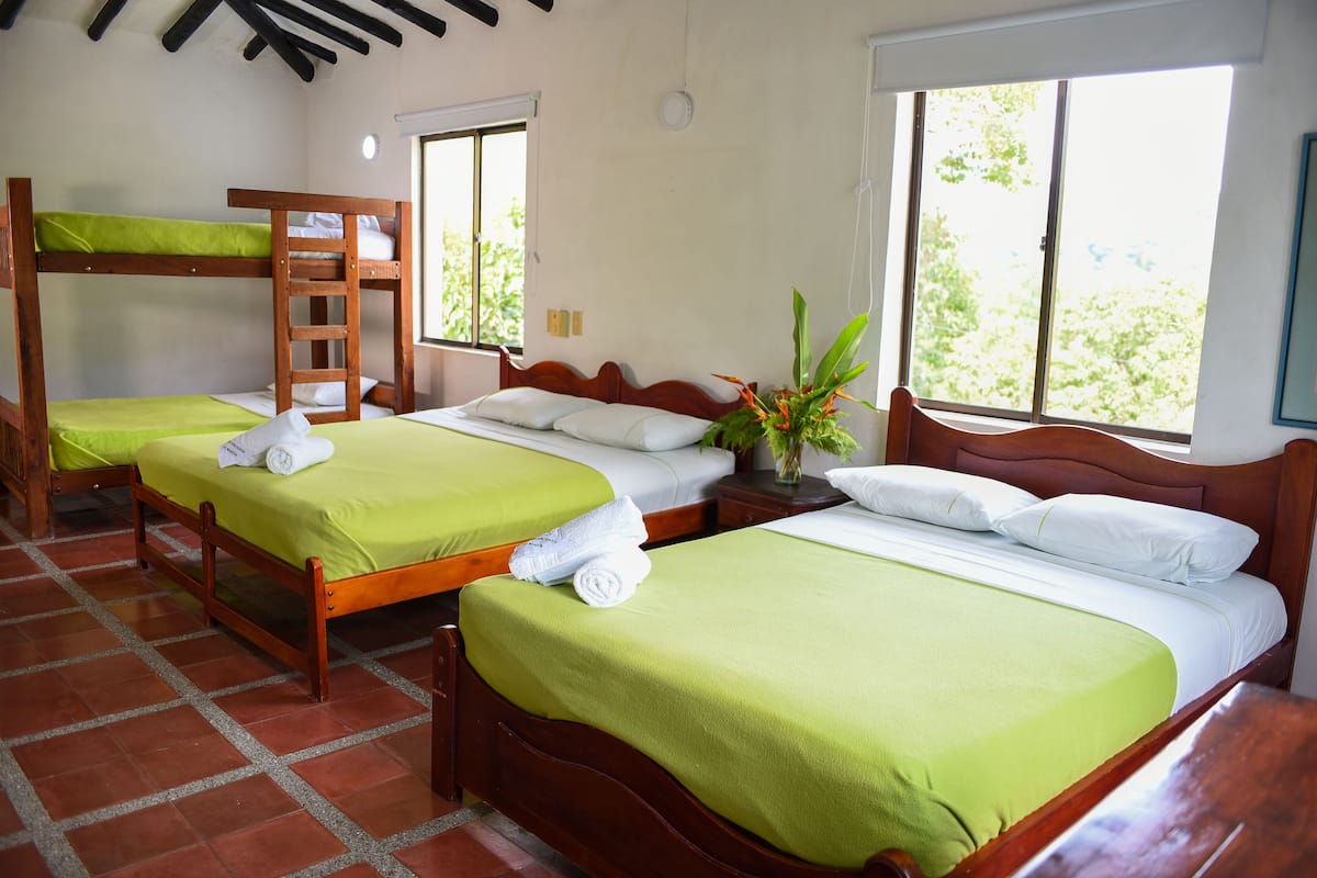 Una habitación de hotel con dos camas de madera, cada una con un edredón verde y almohadas blancas, y una escalera de madera unida a una de las camas.