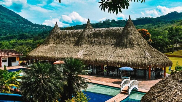Un resort con una cabaña de techo de paja, piscina y palmeras.