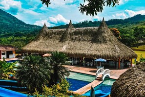 Un resort con una cabaña de techo de paja, piscina y palmeras.