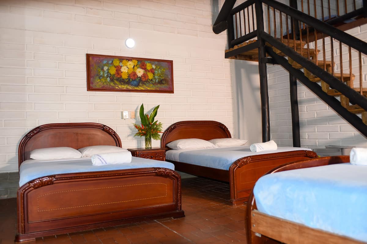 Una habitación de hotel con dos camas de madera, una pared de ladrillo blanco, un cuadro y una escalera.
