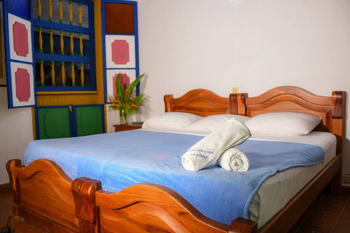 Una cama bien hecha con una colcha azul y una toalla doblada encima.