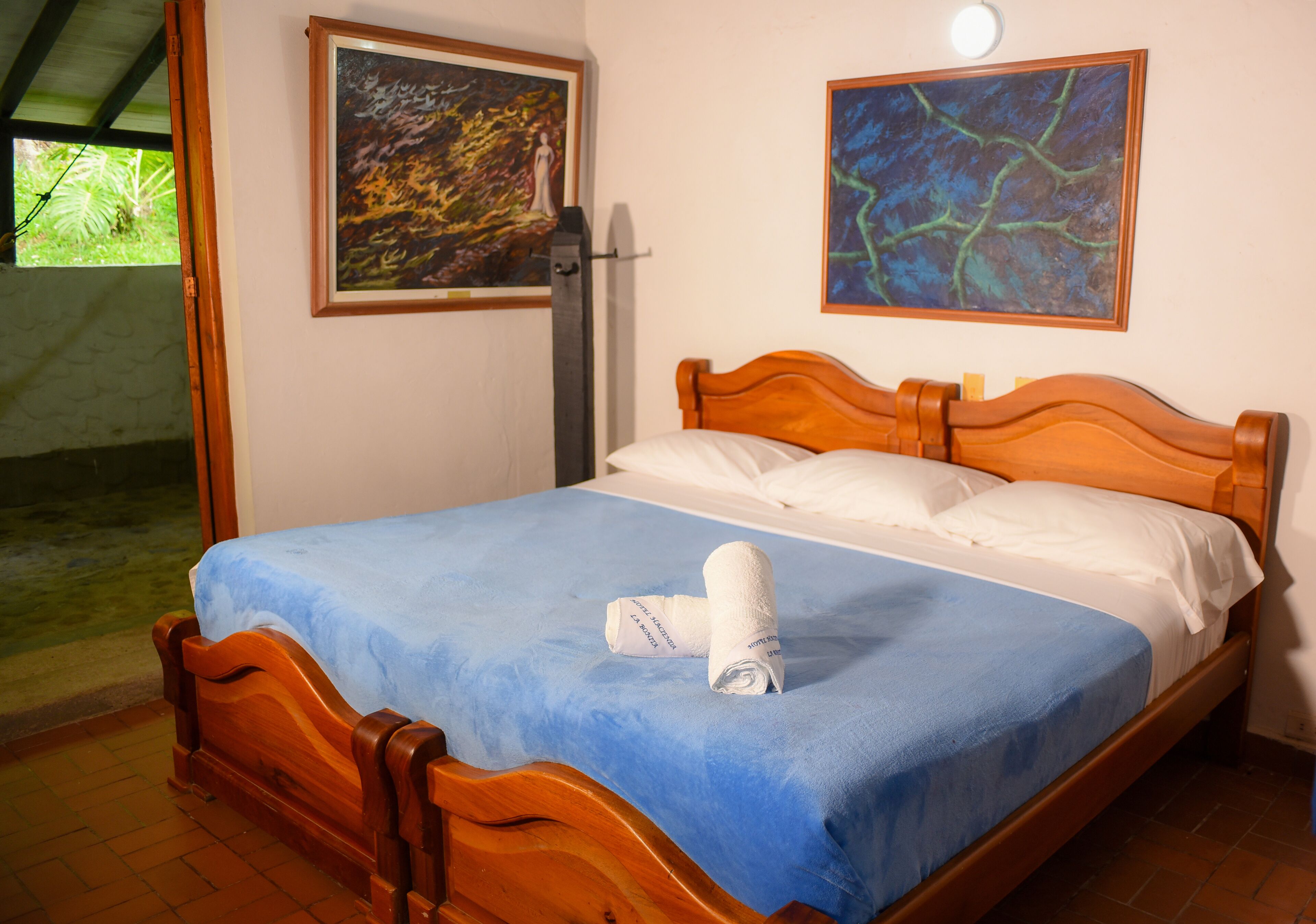 Un lit bien fait, avec une couvre-lit bleue et des oreillers blancs, une tête de lit en bois et deux tableaux accrochés aux murs.