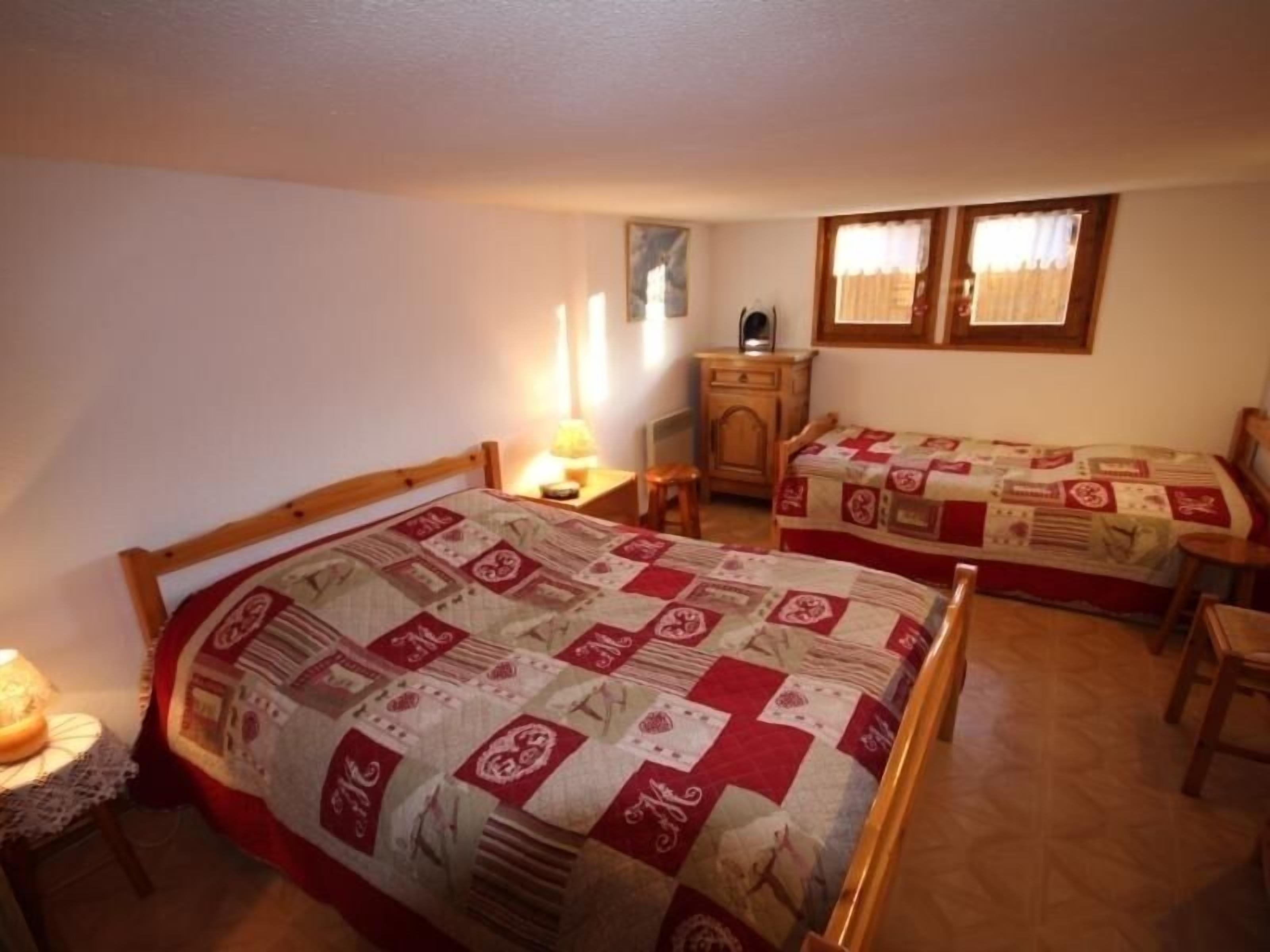 A bedroom with two single beds, a nightstand with a lamp, a wooden dresser, and a window with curtains.