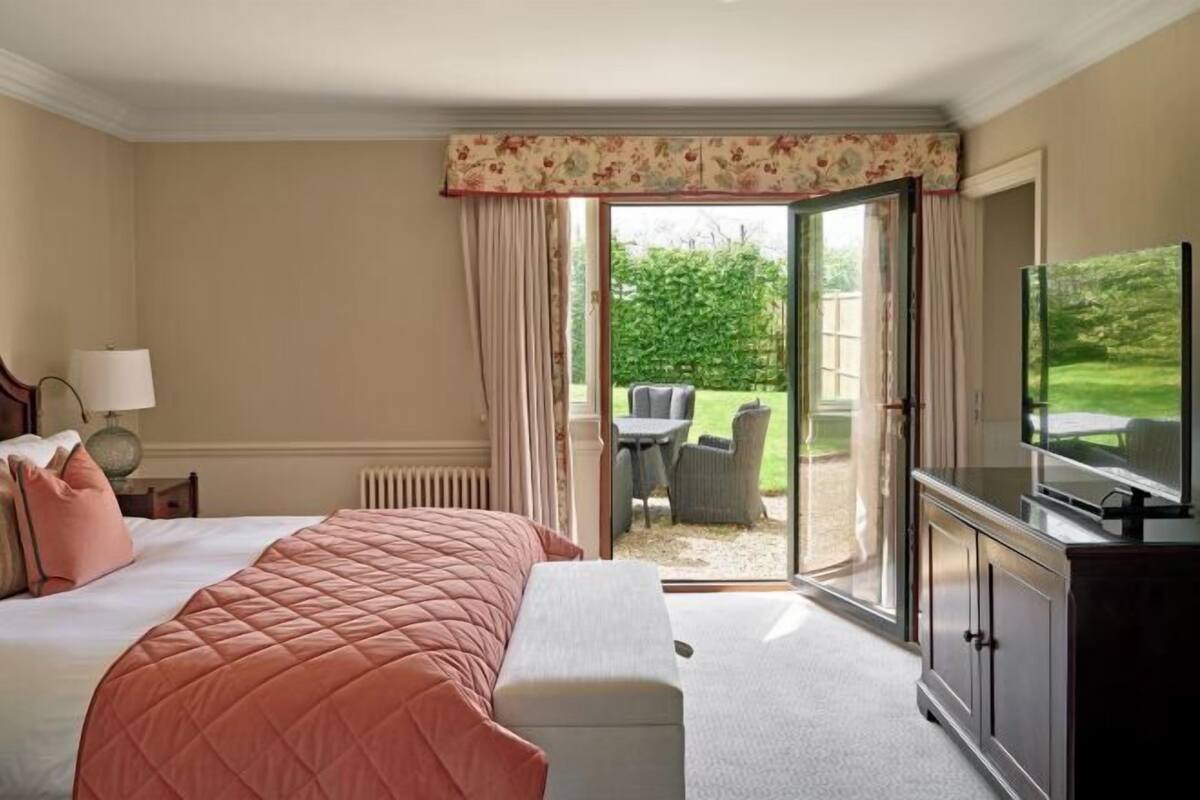 A hotel room with a bed, a TV, a desk, and a view of a garden through a sliding glass door.