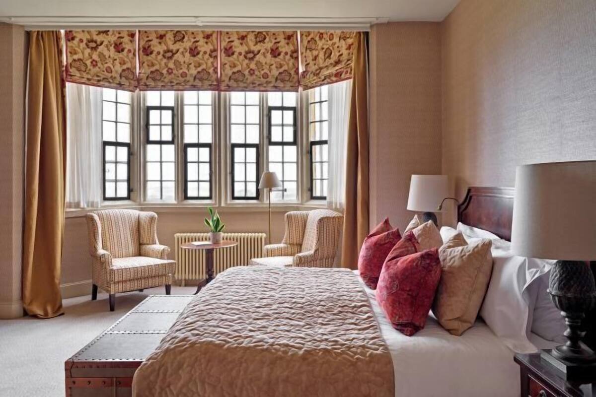 A hotel room with a large bed, two armchairs, a small table, and a window with curtains.