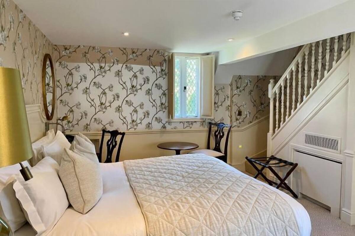 A hotel room with a large bed, a small table, a chair, and a staircase.