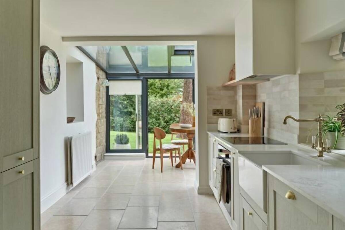 A modern kitchen with a large window, a dining area with a table and chairs, and a view of greenery outside.