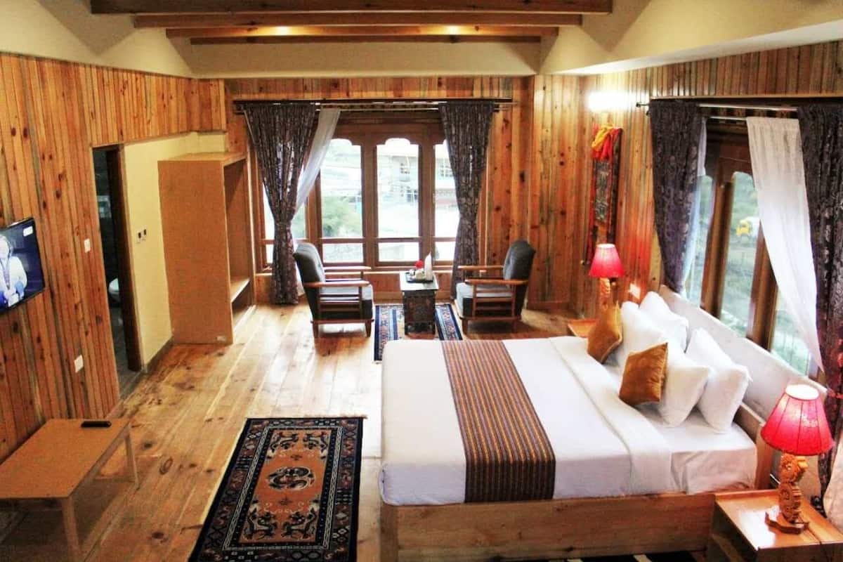 A wooden-themed room with a bed, a TV, a desk, and a window with curtains.