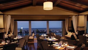 A restaurant with tables set for dining, large windows offering a view of the cityscape, and a wooden ceiling.