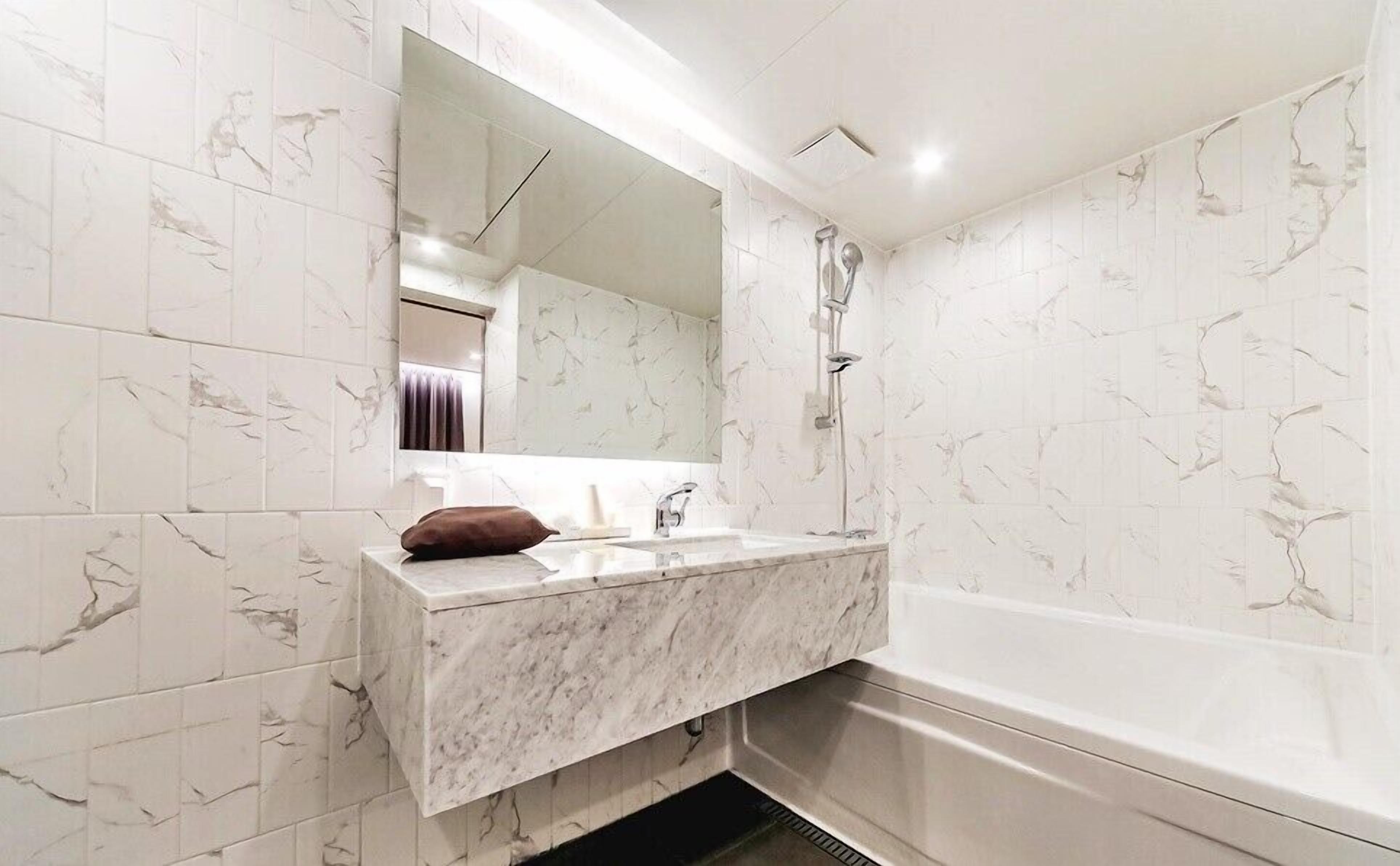 A bathroom with a marble sink, a large mirror, and a bathtub.