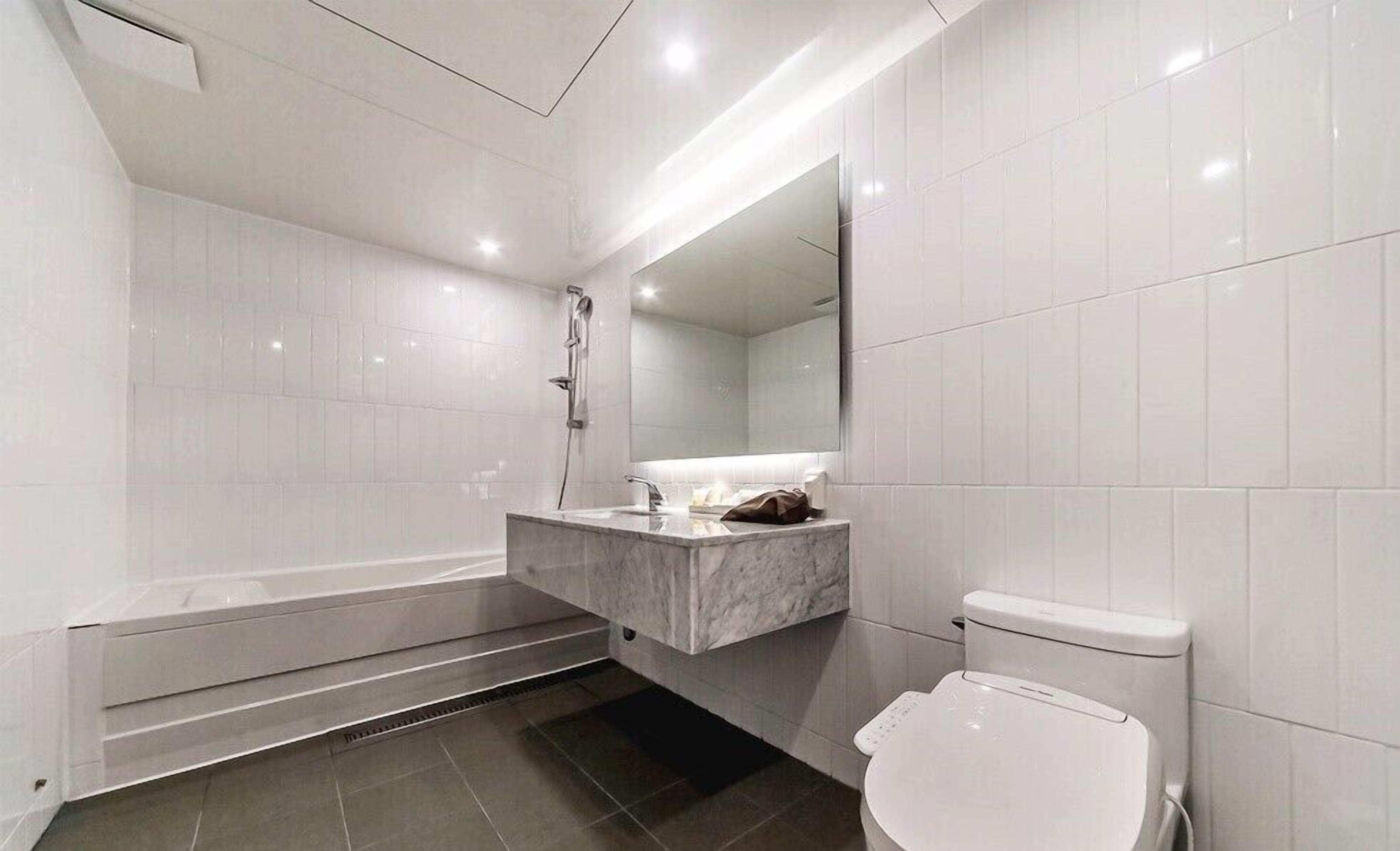 A modern bathroom with a bathtub, a toilet, and a vanity with a mirror.