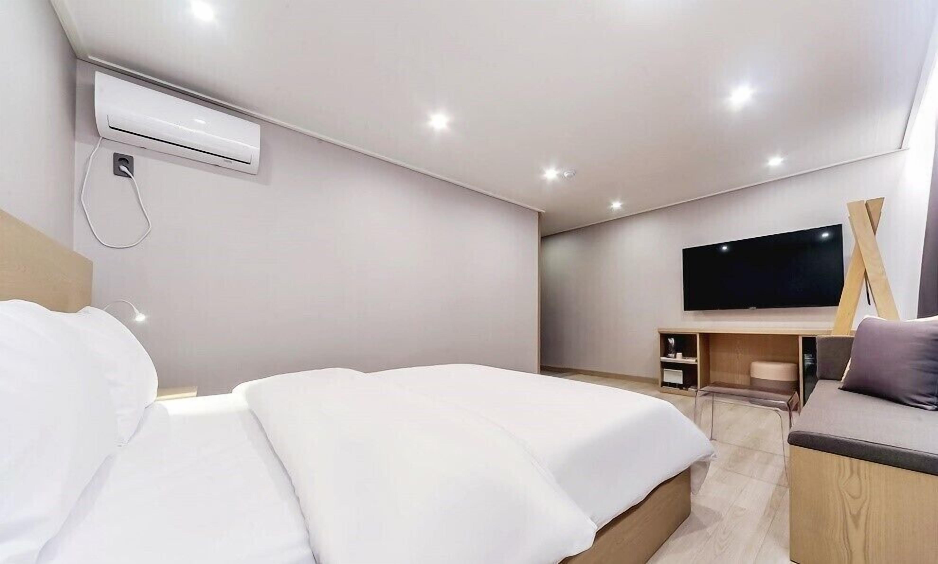 Una habitación de hotel moderna con una cama, un equipo de aire acondicionado, un televisor y un escritorio de madera.