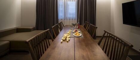 Ein Essbereich mit einem langen Holztisch, Stühlen, einer Couch und einem an der Wand befestigten Fernseher.