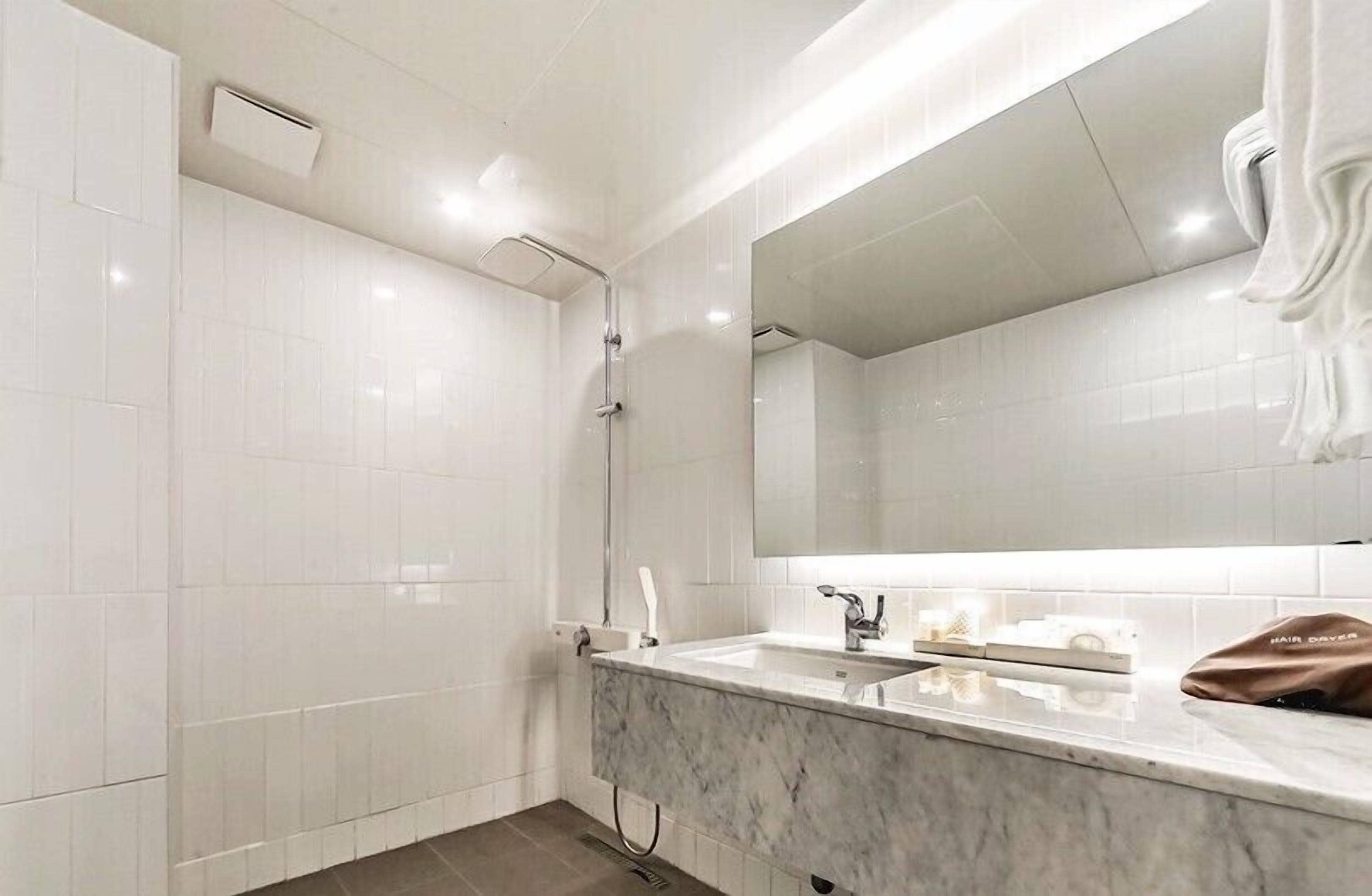 A modern bathroom with white tiles, a marble sink, a large mirror, and a hair dryer on the counter.