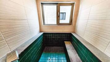 Un baño pequeño y estrecho con ventana, piso de baldosas verde y negro, y paredes de color claro.
