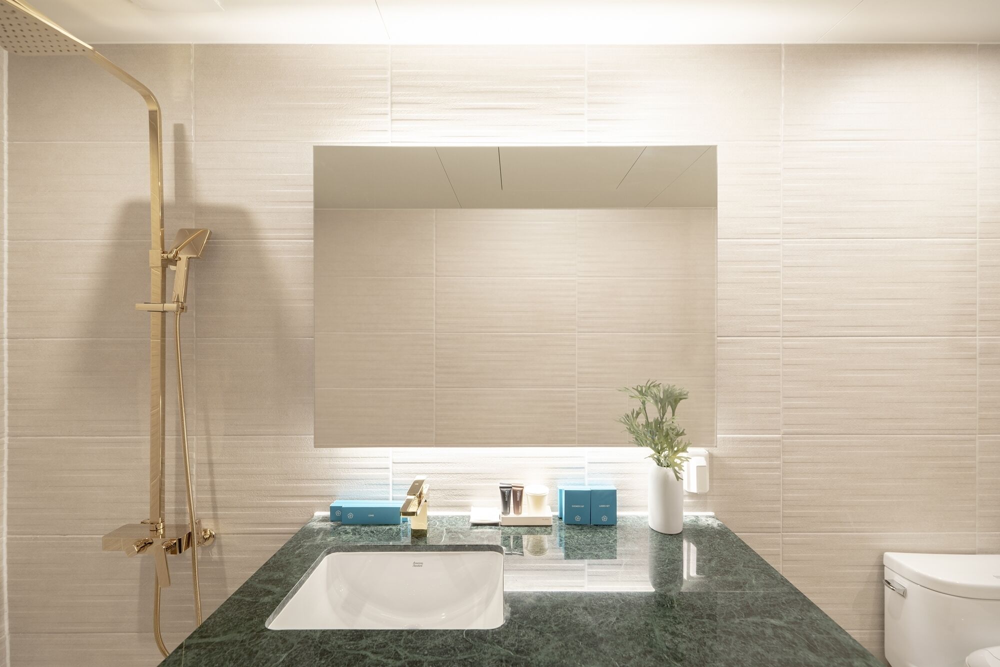 A bathroom with a large mirror, a shower with a gold fixture, a sink with a marble countertop, and a toilet.